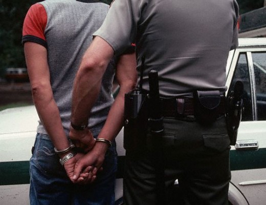 August 1983, Yosemite National Park, California, USA --- A ranger takes a handcuffed and arrested camper to the patrol car. The camper, who is very likely intoxicated, was arrested after complaints of disorderly conduct were made against him. Yosemite National Park, California --- Image by © Jonathan Blair/Corbis