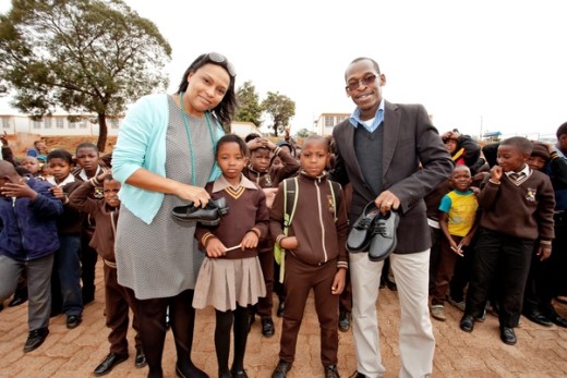 Megan Meas, regional marketing manager of Sandton City and Nelson Mandela Square, and Tshepo Monnamoroe, operations manager of Eastgate Shopping Centre, give shoes to two Munsieville Primary school-goers.